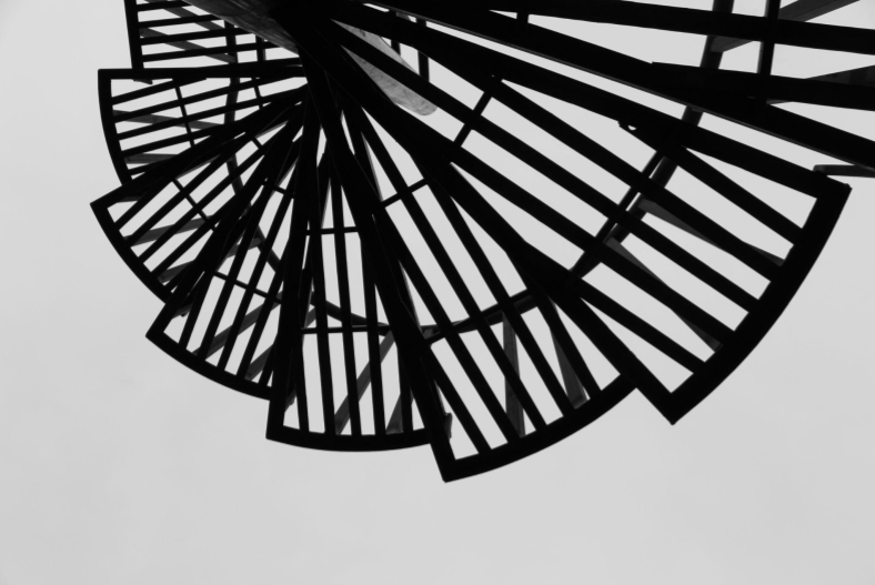 Photographie en noir et blanc montrant une structure métallique en spirale vue en contre-plongée, effet graphique abstrait.