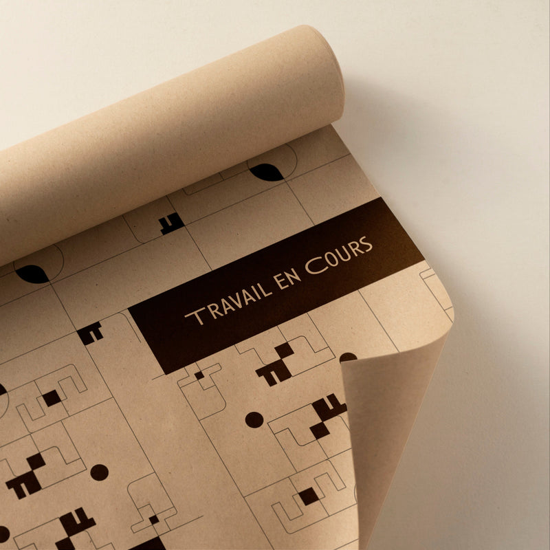 Affiche “Travail en cours” sur papier kraft vue de près, avec motifs géométriques et bande brune typographique.