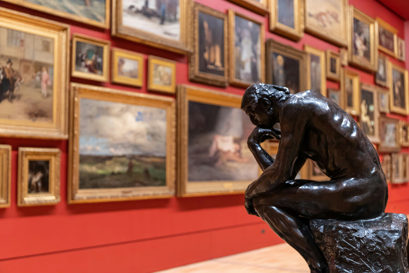 Sculpture Le Penseur de Rodin dans une galerie d'art avec mur rouge et collection de tableaux encadrés